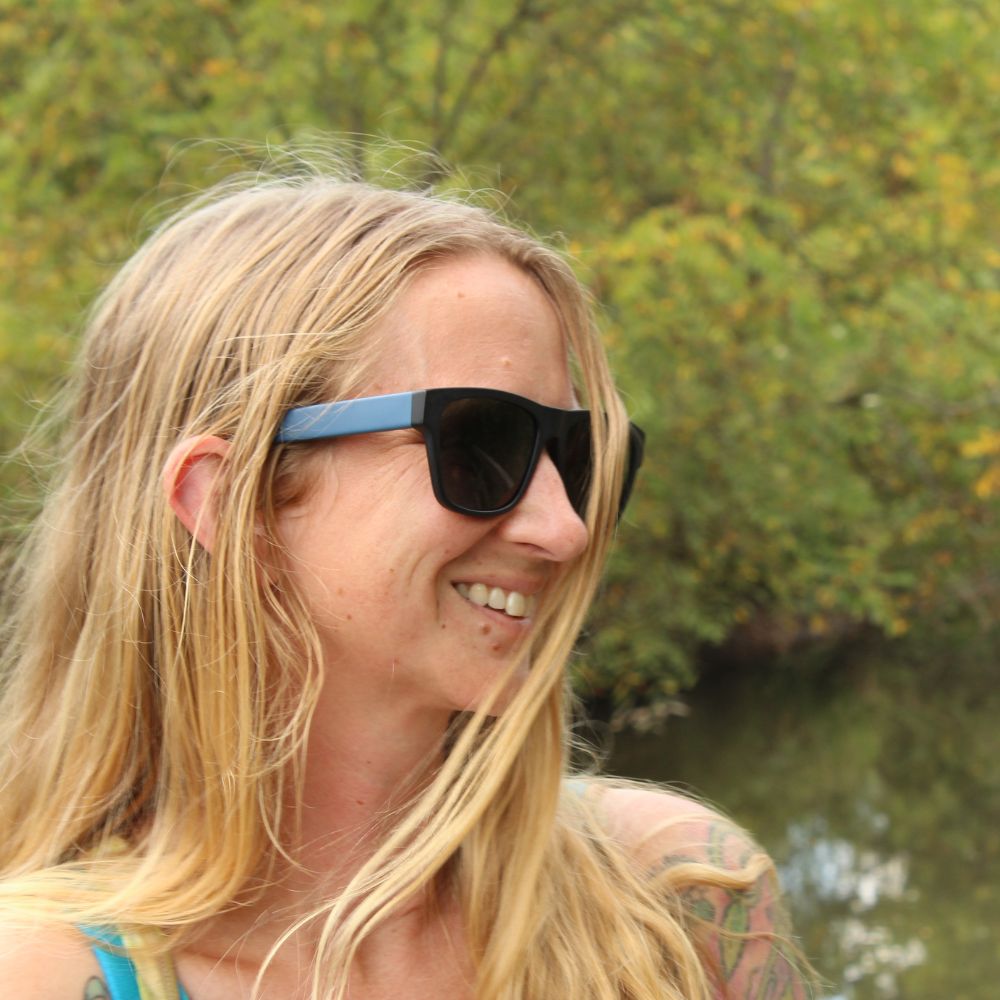 Blue square acetate sunglasses with green lens on woman by lake